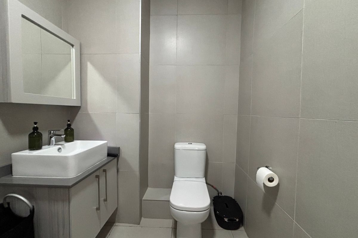A modern bathroom featuring a vanity cabinet with a countertop basin, wall-mounted mirror, and a standard toilet, finished with neutral wall and floor tiles.