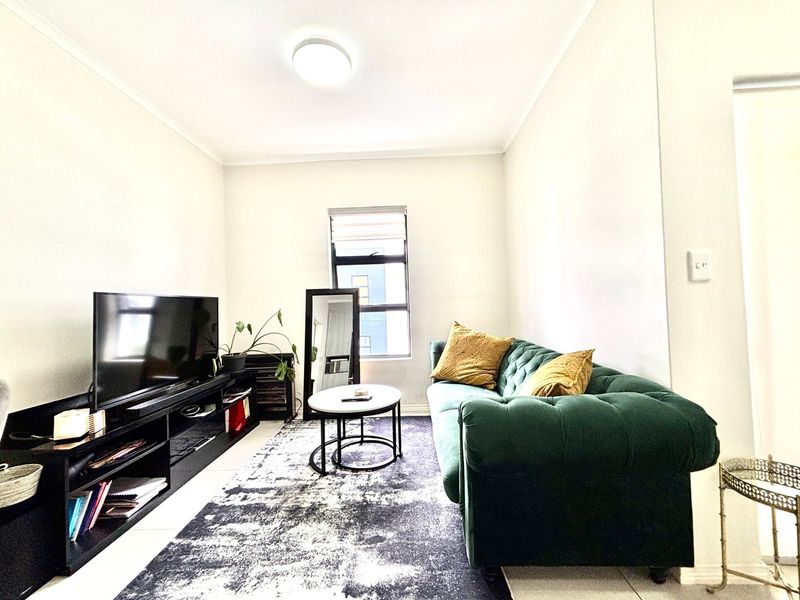 A bright living room featuring tiled flooring, a central flush mount ceiling light, and a window with a fitted roller blind.