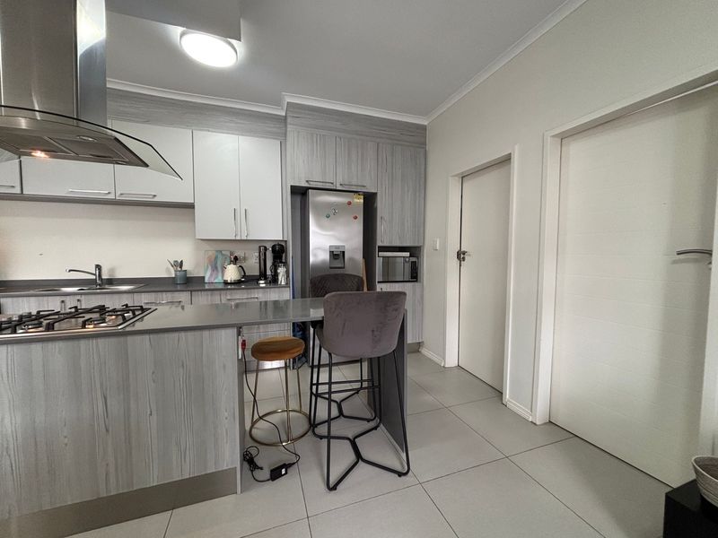 Modern kitchen featuring light wood-grain cabinetry, stone countertops, a gas hob with extractor fan, and integrated appliances, finished with neutral floor tiles.