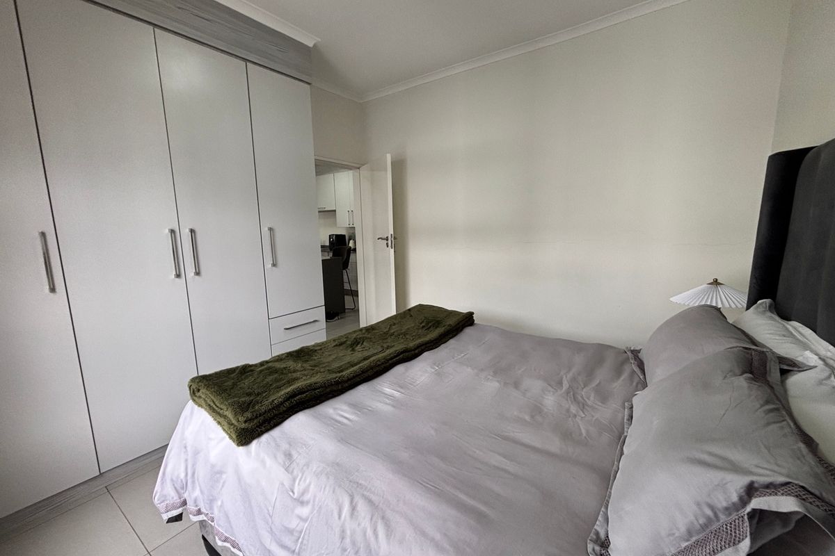 A well-maintained bedroom featuring neutral tiled flooring, ample built-in cupboard storage, and a clean, modern aesthetic.