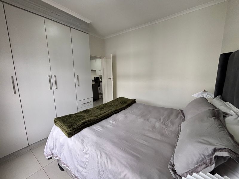A well-maintained bedroom featuring neutral tiled flooring, ample built-in cupboard storage, and a clean, modern aesthetic.