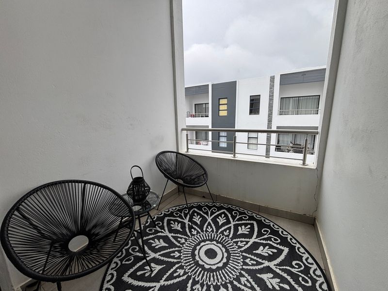 A compact apartment balcony featuring a stainless steel balustrade and tiled flooring, offering an urban view of the surrounding residential complex.