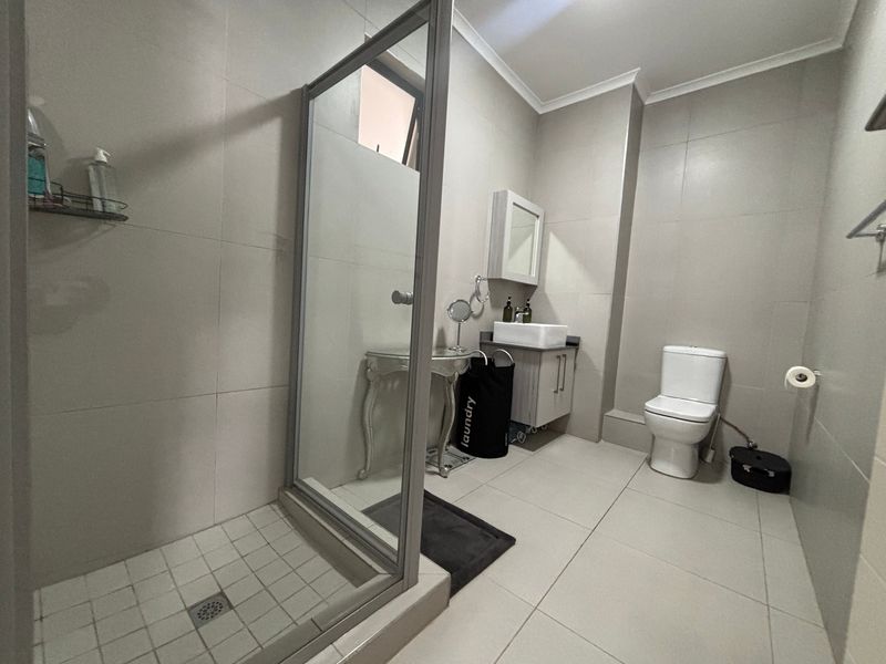 A modern bathroom featuring a glass-enclosed shower, a vanity with a vessel sink, and neutral floor-to-ceiling tiling.