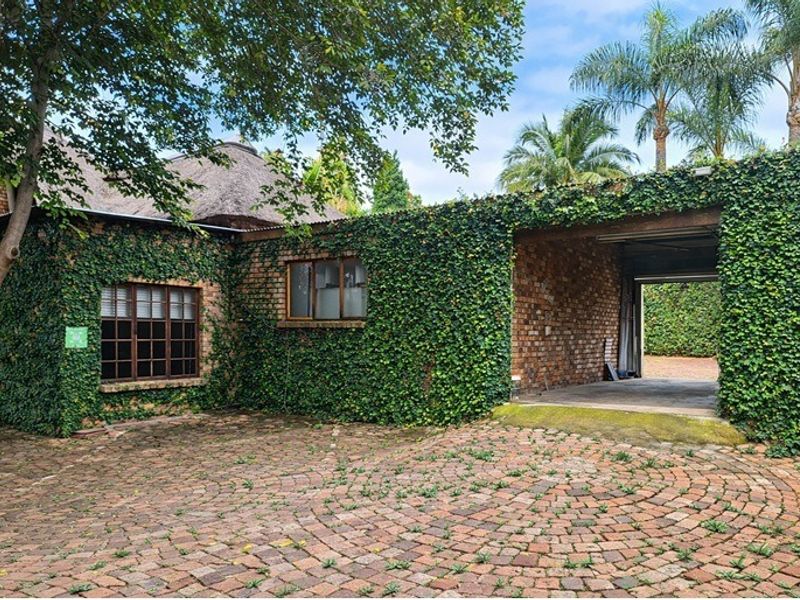 Front exterior view of a brick house featuring a thatched roof, ivy-covered walls, and a paved driveway leading to a garage.