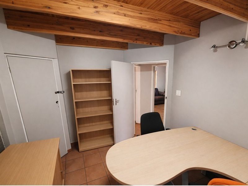A functional home office featuring exposed timber ceiling beams, tiled flooring, and a built-in shelving unit, providing a practical workspace.