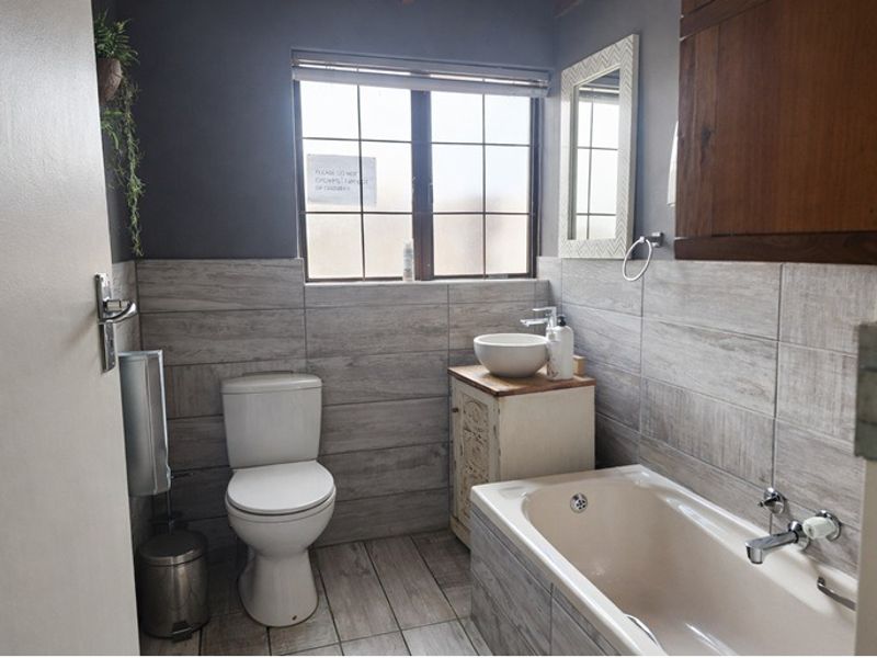 A well-maintained bathroom featuring a bathtub, a vessel sink on a vanity cabinet, and modern wood-look wall and floor tiling.