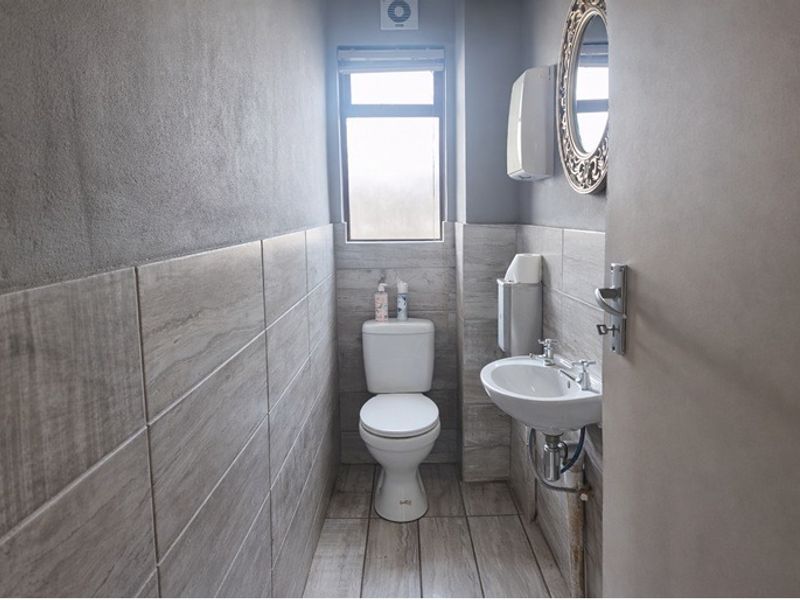 A compact, modern bathroom featuring neutral wood-look floor and wall tiles, a pedestal basin, and a standard toilet.