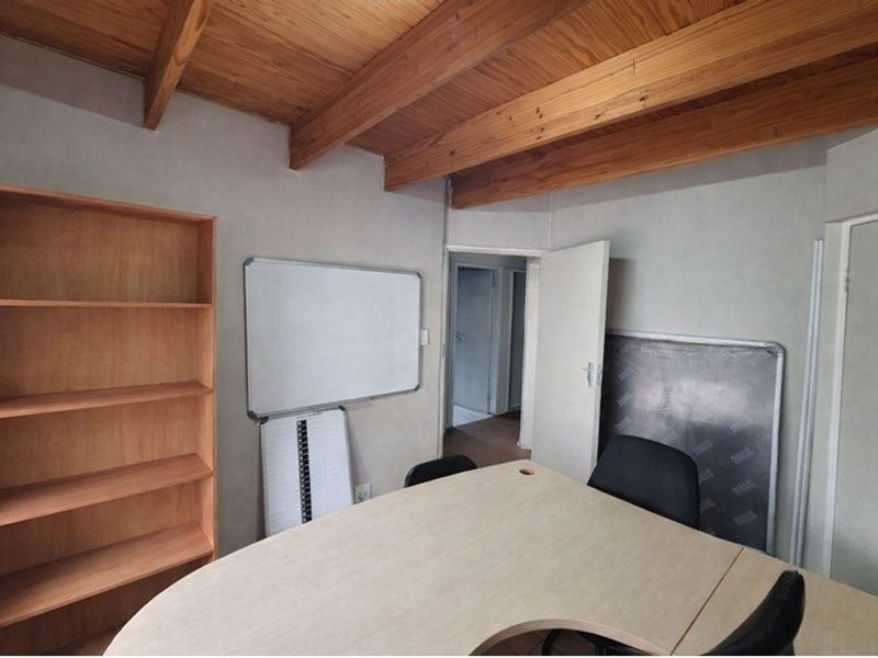 A functional office space featuring exposed timber ceiling beams and a built-in shelving unit, providing a practical workspace environment.