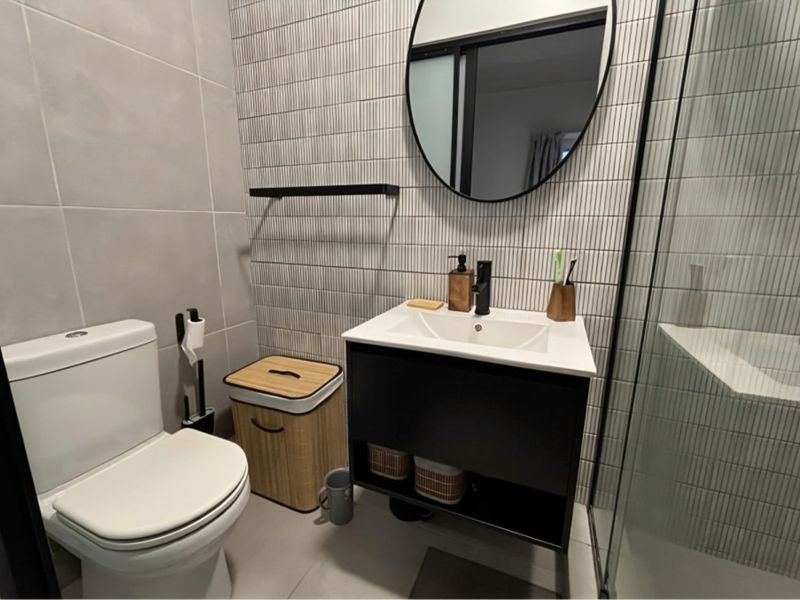 Modern bathroom featuring a sleek vanity cabinet, contemporary wall-mounted mirror, glass shower enclosure, and stylish textured wall tiling.