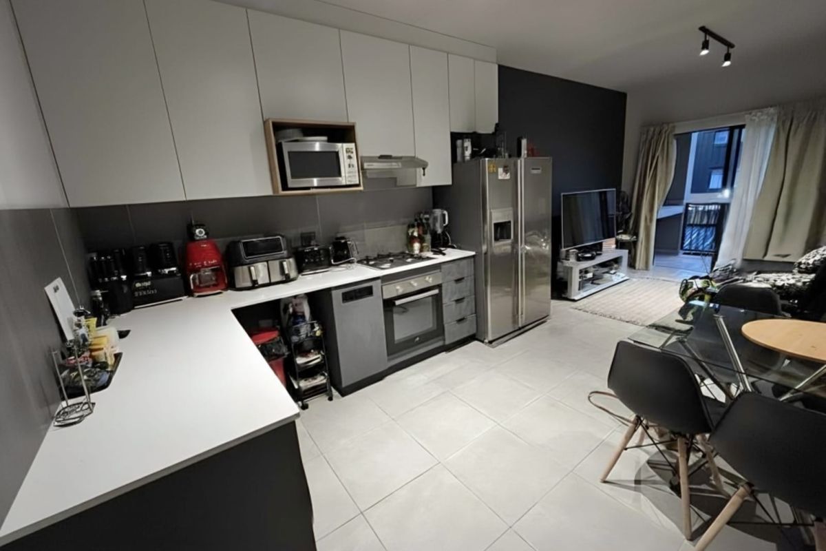 Modern open-plan kitchen and living area featuring sleek cabinetry, integrated appliances, tiled flooring, and direct access to a balcony.