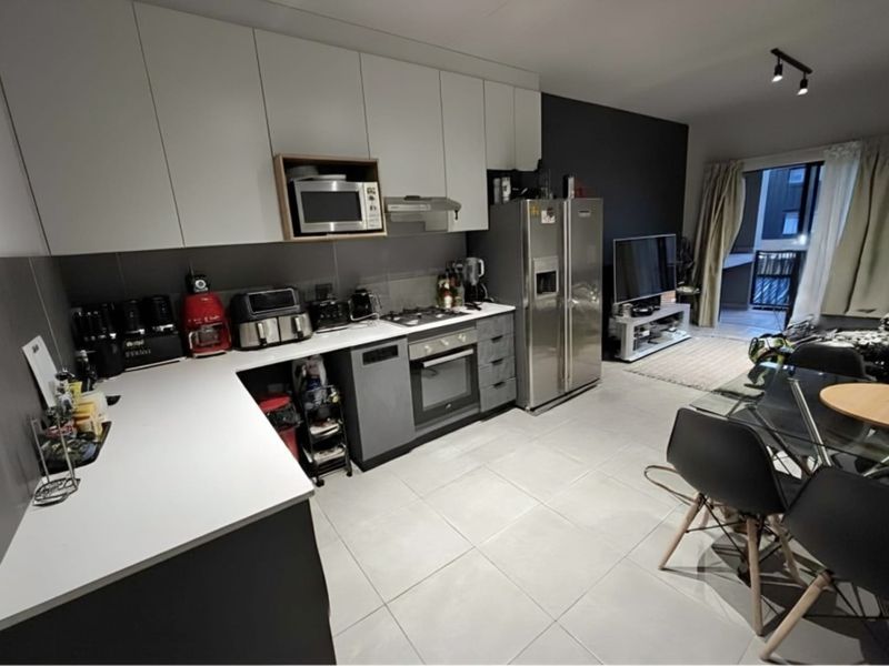 Modern open-plan kitchen and living area featuring sleek cabinetry, integrated appliances, tiled flooring, and direct access to a balcony.