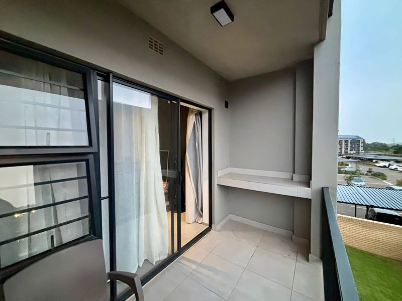A clean, covered balcony featuring tiled flooring, a built-in counter, and sliding glass doors providing access to the interior living space.
