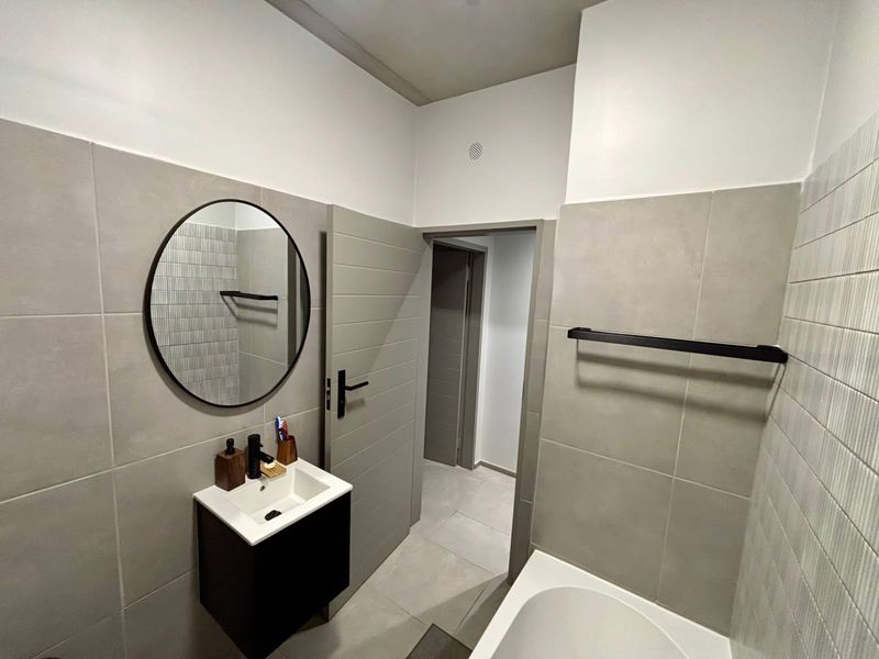 Modern bathroom featuring a wall-mounted vanity with basin, black fixtures, bathtub, and neutral grey tiling throughout.
