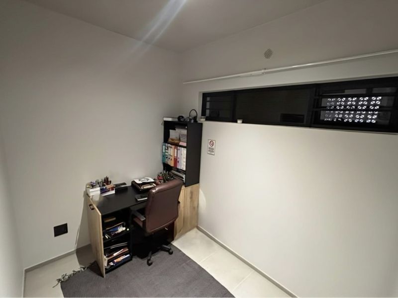 A compact home office space featuring neutral walls, tiled flooring, and a high-level horizontal window providing natural light.