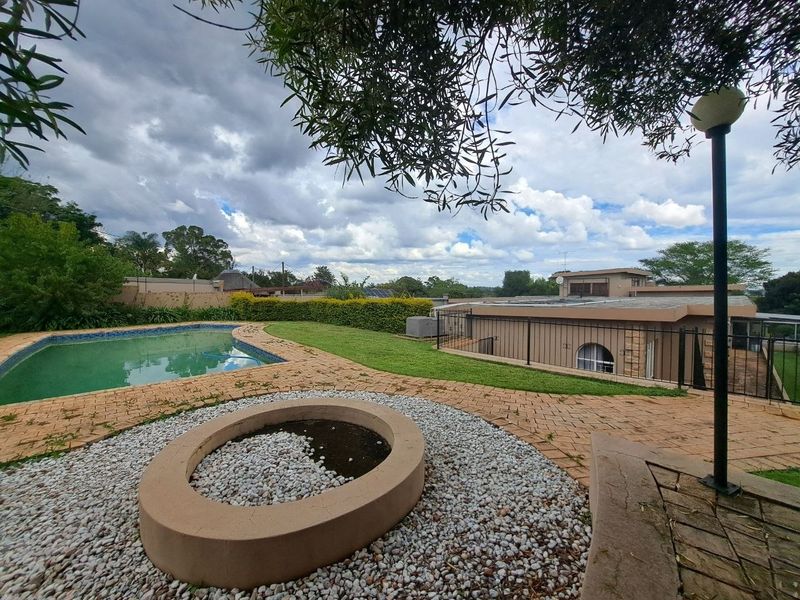 Outdoor entertainment area featuring a swimming pool, paved patio, and a built-in fire pit, set within a landscaped garden with perimeter fencing.