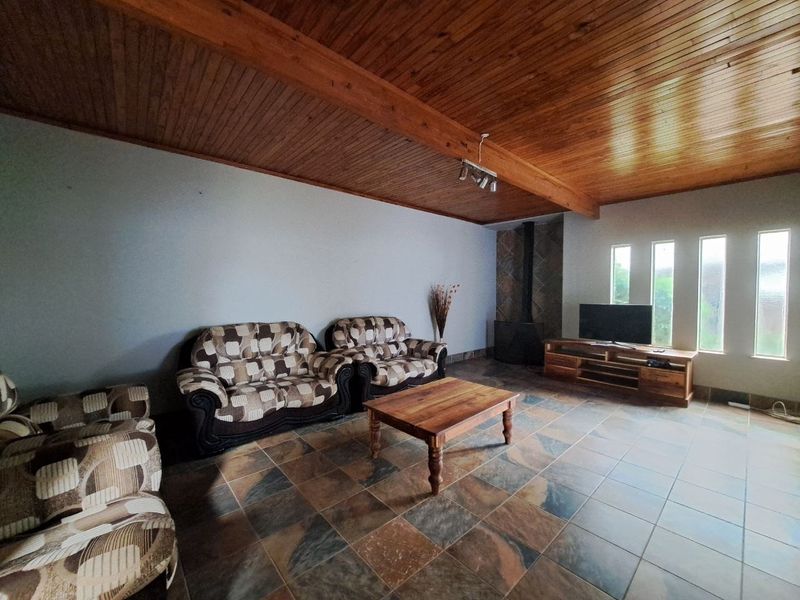 Spacious living room featuring a vaulted timber-clad ceiling with exposed beams, slate tile flooring, and a built-in freestanding fireplace.