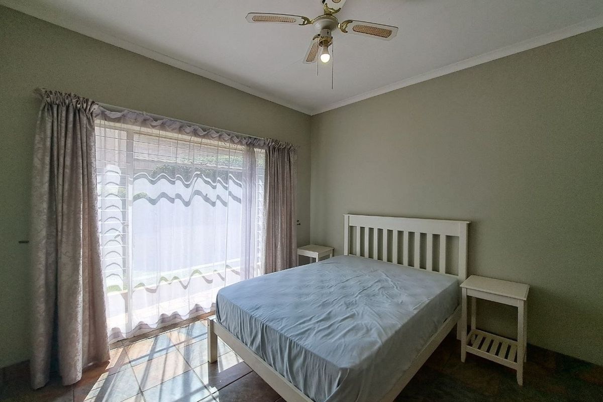 A bedroom featuring tiled flooring, a ceiling fan, and a large sliding glass door providing natural light and access to the exterior.