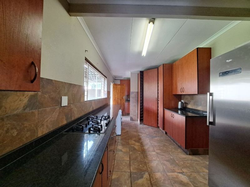A functional kitchen featuring dark granite countertops, wood-finish cabinetry, a gas hob, and tiled flooring throughout.