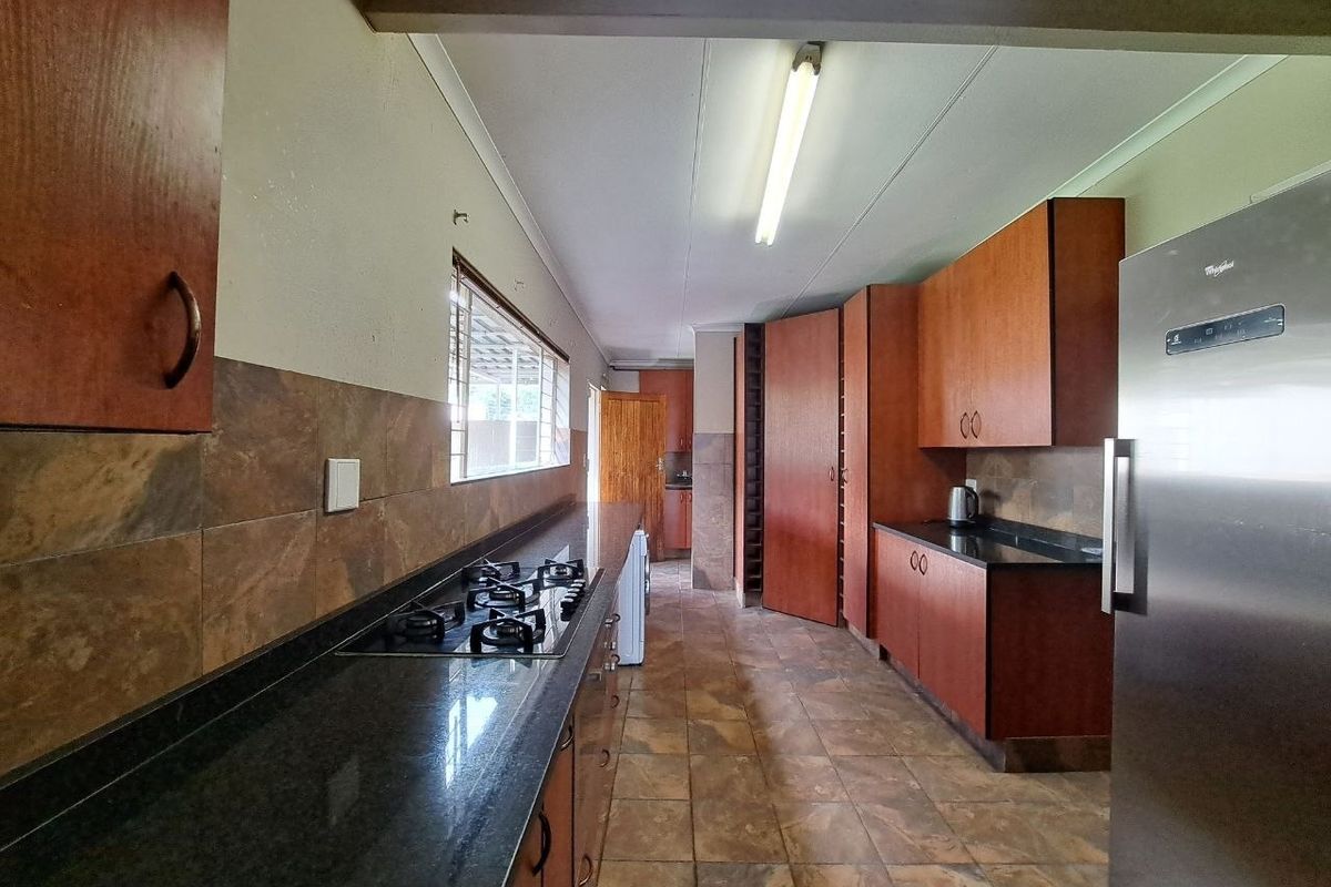 A functional kitchen featuring dark granite countertops, wood-finish cabinetry, a gas hob, and tiled flooring throughout.