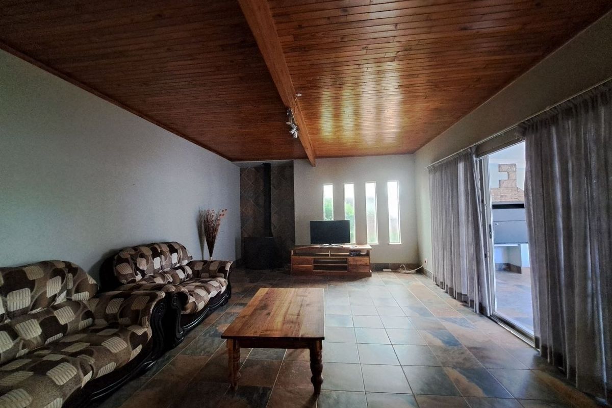 Spacious living room featuring a warm wood-paneled ceiling, tiled floors, a built-in fireplace, and large sliding doors providing access to the outdoor area.