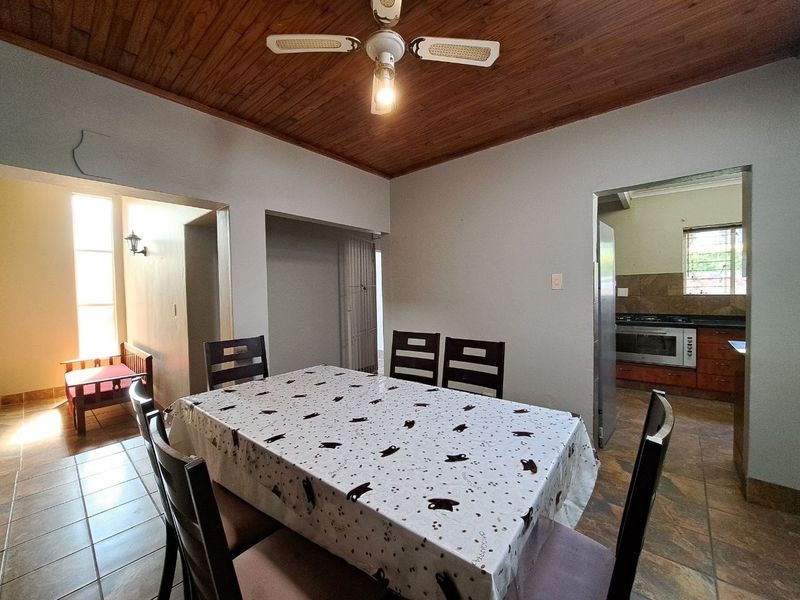 Open plan dining area featuring a timber ceiling and ceiling fan, with an adjacent kitchen visible through the doorway.