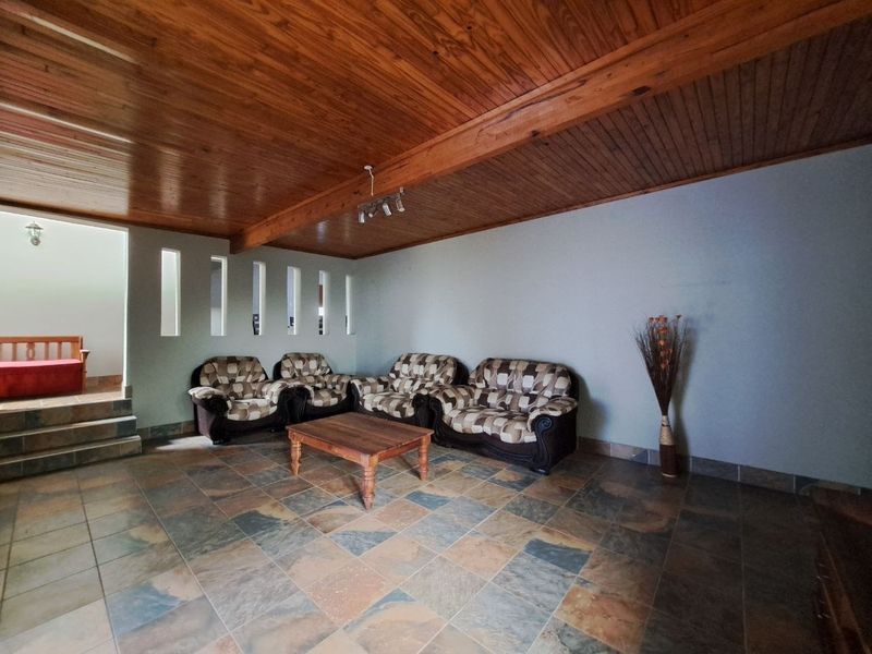 Spacious living area featuring a warm timber tongue and groove ceiling, exposed beam, and durable slate tile flooring with unique feature wall cutouts.