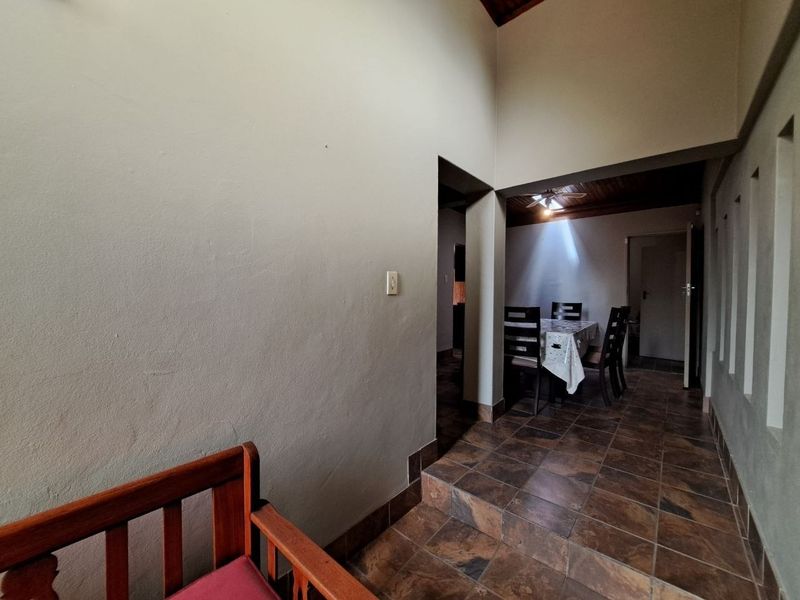 A spacious hallway featuring tiled flooring and a high vaulted ceiling with timber paneling, leading into an adjacent dining area.
