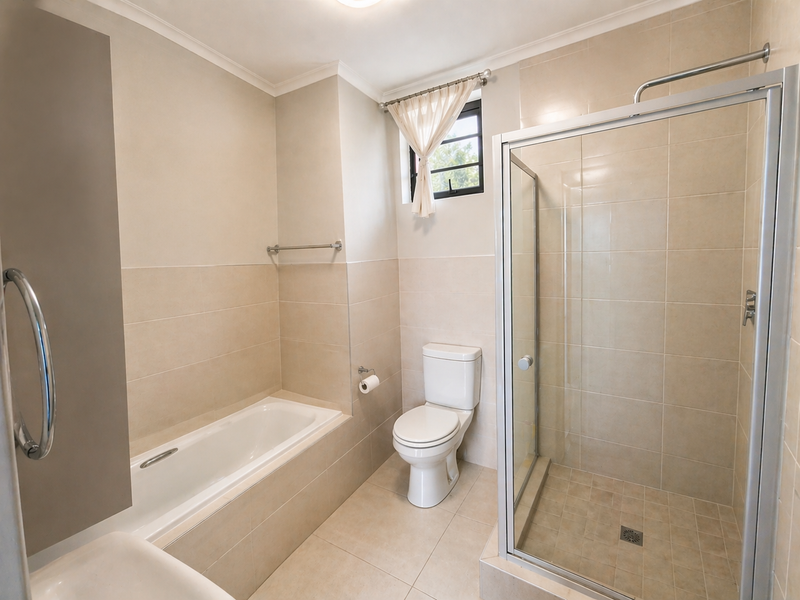 A clean, neutral-toned bathroom featuring a built-in bathtub, a separate glass-enclosed shower, and a standard toilet with tiled finishes throughout.