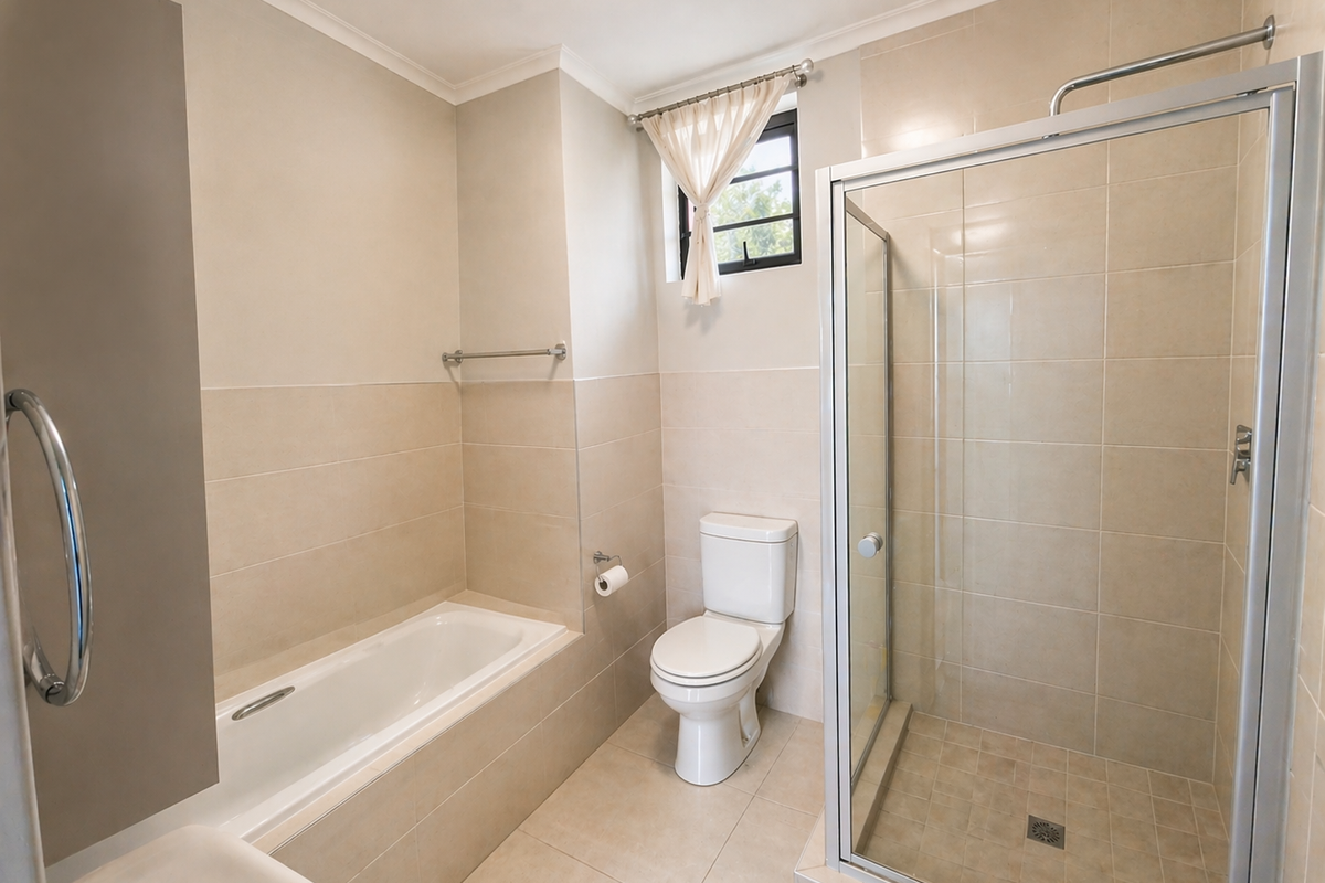 A clean, neutral-toned bathroom featuring a built-in bathtub, a separate glass-enclosed shower, and a standard toilet with tiled finishes throughout.