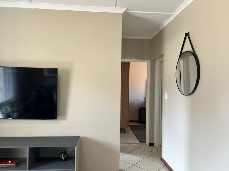 A view of the living area featuring neutral wall tones, tiled flooring, and a coved ceiling, leading into a hallway.