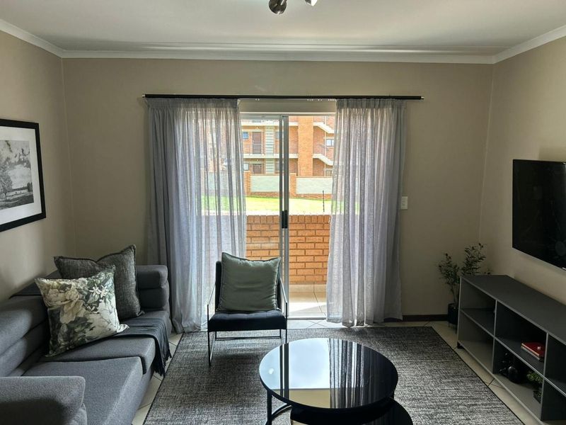 A well-maintained living room featuring tiled flooring, neutral wall tones, and a sliding glass door providing access to an outdoor balcony area.