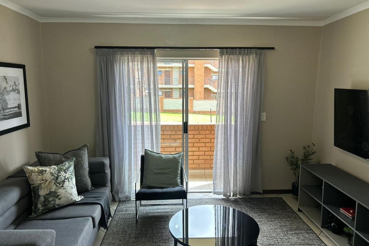 A well-maintained living room featuring tiled flooring, neutral wall tones, and a sliding glass door providing access to an outdoor balcony area.
