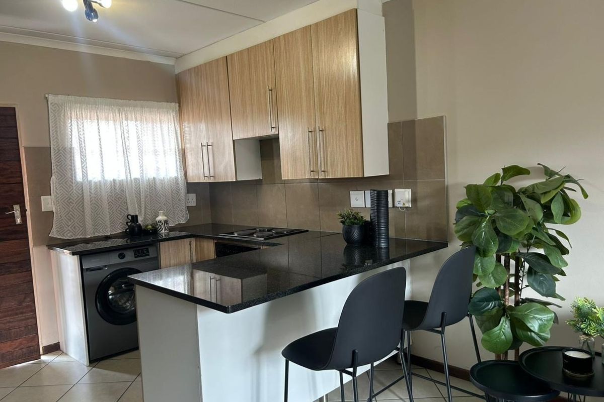 A functional kitchen featuring laminate cabinetry, granite countertops, a tiled backsplash, and a breakfast bar, with integrated space for laundry appliances.