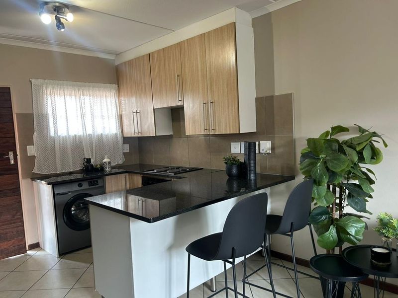 A functional kitchen featuring laminate cabinetry, granite countertops, a tiled backsplash, and a breakfast bar, with integrated space for laundry appliances.