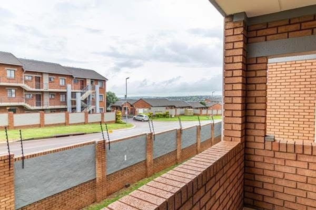 A covered balcony featuring face brick construction, overlooking the complex grounds and perimeter wall with electric fencing.