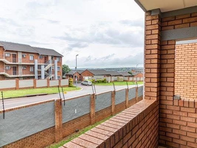 A covered balcony featuring face brick construction, overlooking the complex grounds and perimeter wall with electric fencing.