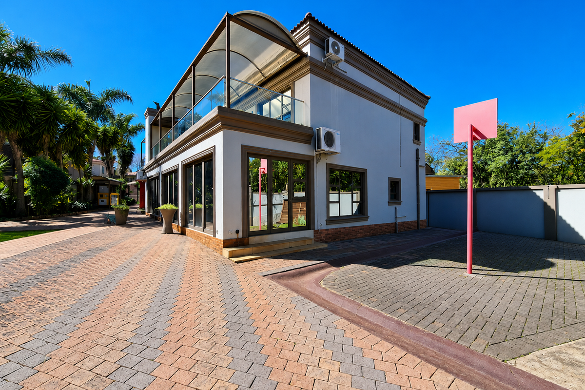Rear exterior view of a two-story house featuring a paved driveway, covered balcony with glass balustrade, and wall-mounted air conditioning units.