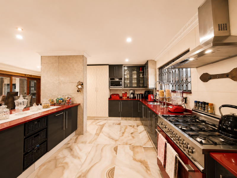 Modern kitchen featuring dark cabinetry, contrasting red countertops, large format marble-look floor tiles, and high-end stainless steel gas cooking appliances.