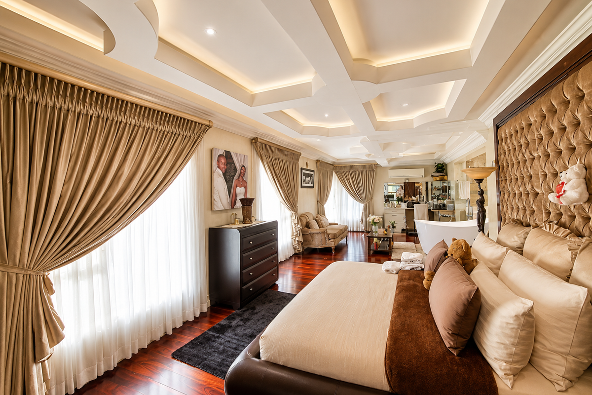Spacious master bedroom featuring a coffered ceiling with recessed lighting, rich hardwood flooring, and an integrated en-suite area with a freestanding bathtub.