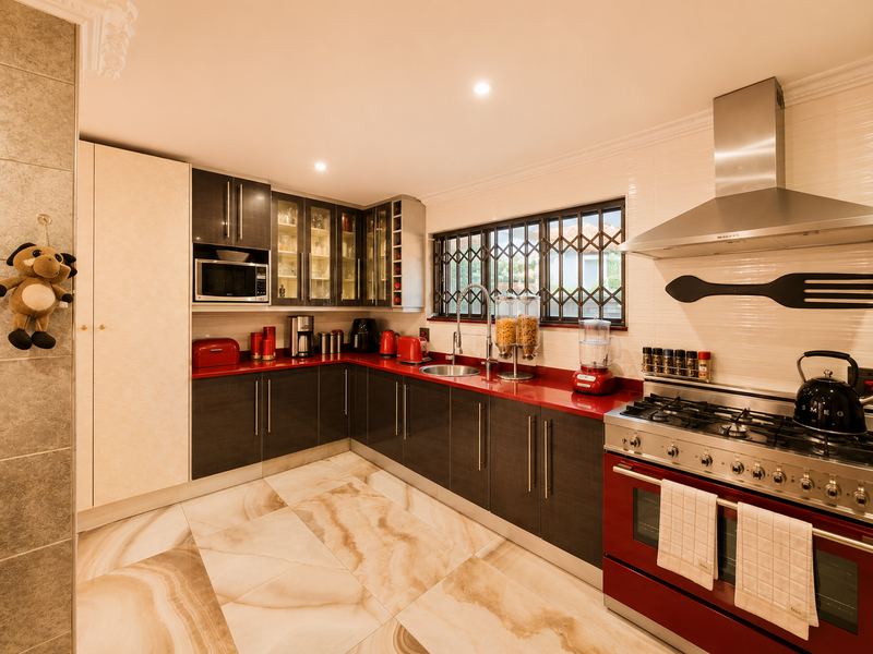 Modern kitchen featuring dark cabinetry, red countertops, a large stainless steel gas range with extractor hood, and polished marble-look floor tiles.