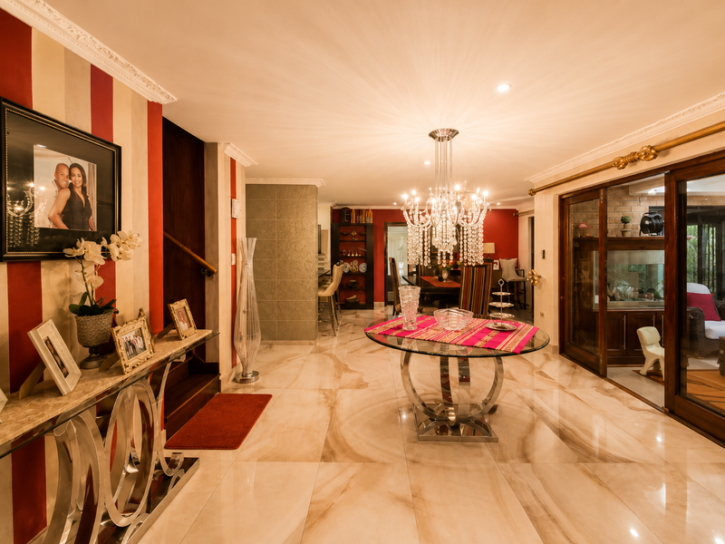 Spacious open-plan living area featuring polished marble flooring, elegant crown molding, and a striking crystal chandelier, with seamless access to the outdoor patio.