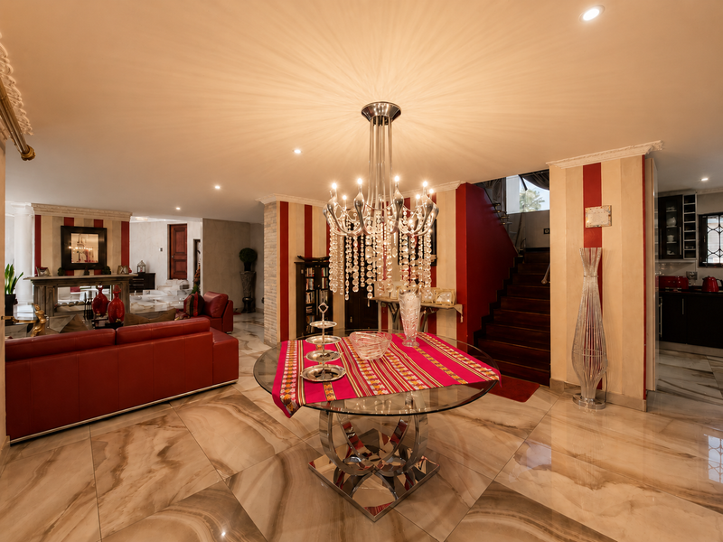 Spacious open-plan living and dining area featuring polished marble flooring, a grand crystal chandelier, and a staircase leading to the upper level.