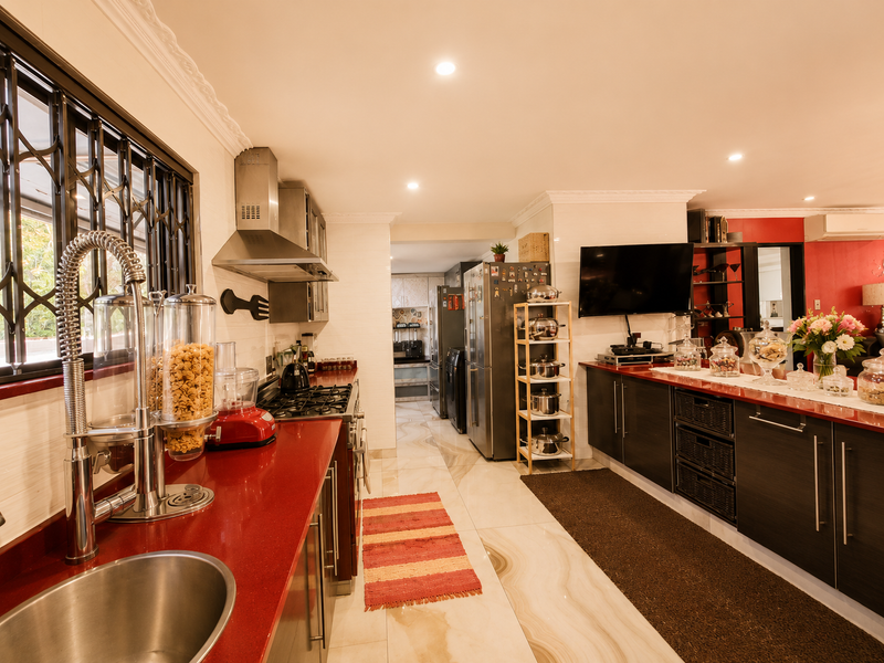 Modern kitchen featuring red stone countertops, dark cabinetry, gas hob, extractor fan, and polished tile flooring with a view into a secondary scullery area.