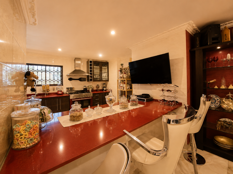A well-lit kitchen featuring a prominent red stone breakfast bar, stainless steel gas range, extractor fan, and ample built-in cabinetry with decorative crown molding.