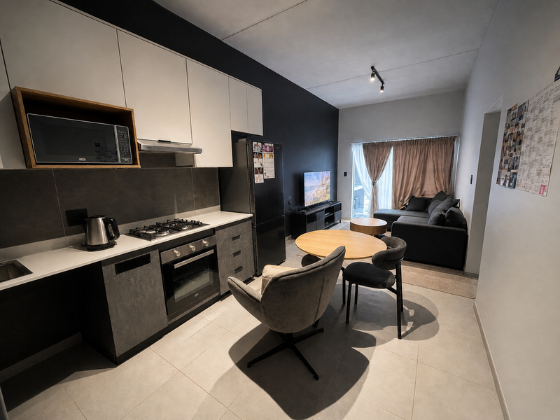 Modern open-plan apartment featuring a sleek kitchen with built-in appliances, tiled flooring, and a seamless transition to the living area with balcony access.