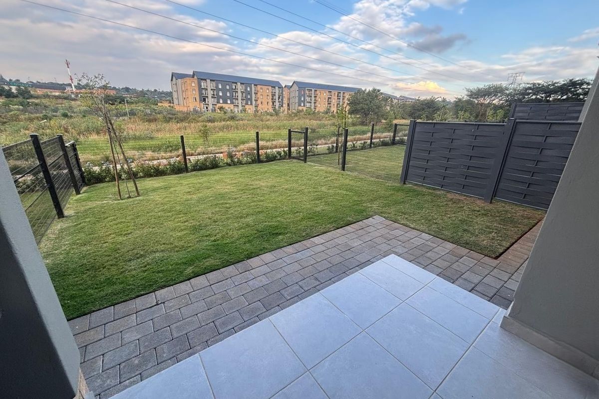 A well-maintained rear garden featuring a paved patio area, neat lawn, and modern perimeter fencing with open views of the surrounding estate.