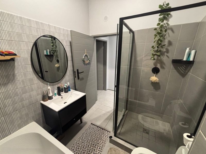 Modern bathroom featuring a sleek vanity unit, a walk-in shower with a black-framed glass screen, and contemporary grey wall tiling.