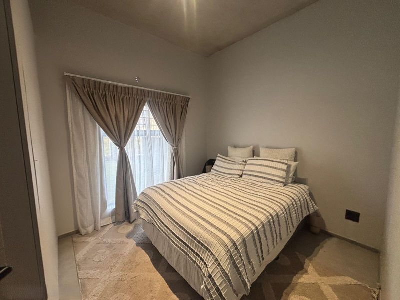 A well-lit bedroom featuring neutral walls, tiled flooring, and a sliding glass door providing access to the exterior.