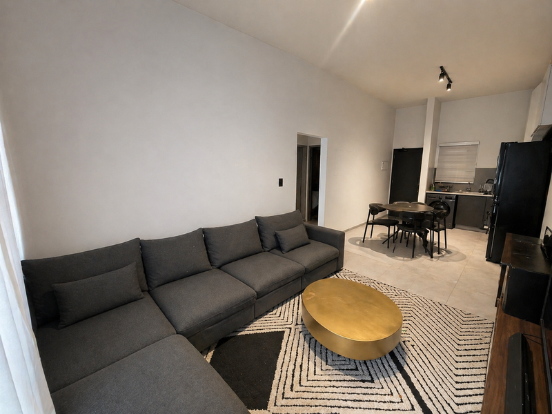 An open-plan living and kitchen area featuring tiled floors, modern track lighting, and a functional kitchen layout with built-in cabinetry.