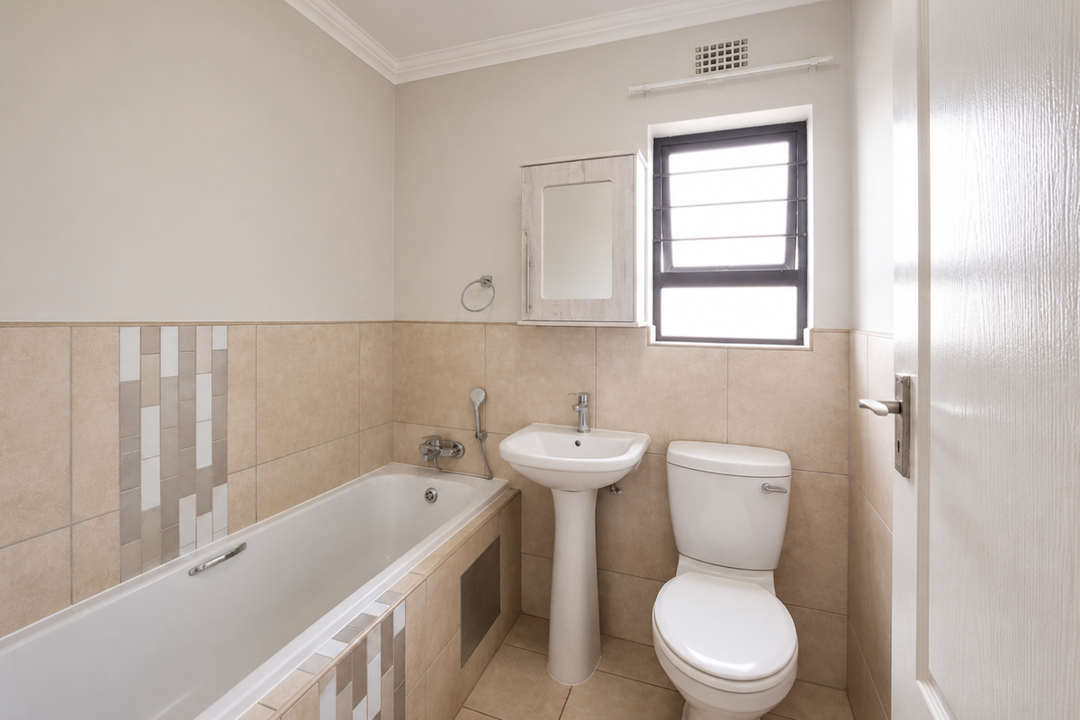 A clean, well-maintained bathroom featuring a bathtub, pedestal basin, toilet, and neutral wall tiling with decorative accents.